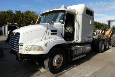 Mack CXN613 conventional sleeper truck in a yard, front-left view, white cab with sleeper, fuel tanks, and rear wheels visible.