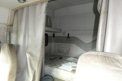 Truck sleeper cab interior showing bed with mattress and small storage compartments
