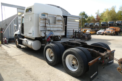 Mack CXN613 tractor truck chassis with cab detached, rear wheels visible, stock yard with equipment in background.