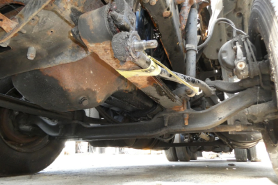 Truck undercarriage view showing suspension and steering components with some rust and wiring visible.