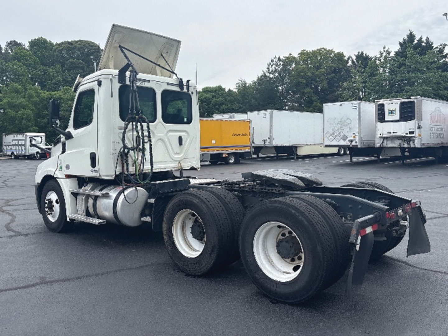Freightliner Cascadia 126 tractor in a used inventory lot, side view showing cab, fuel tanks, and dual rear axles with open frame.