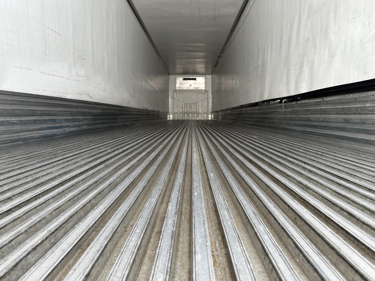Trailer interior showing ribbed load floor in a refrigerated trailer with white walls and a small rear opening glimpse.