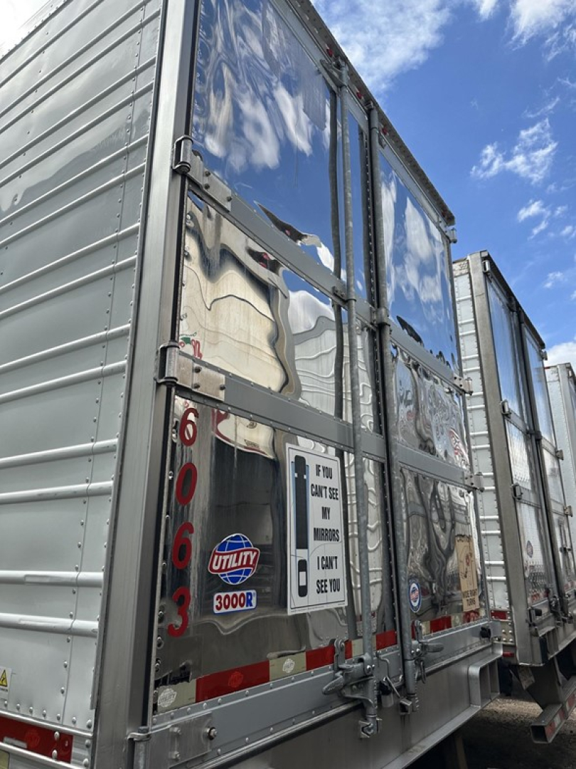 Trailer rear view showing a 2018 Utility 3000R reefer trailer with reflective aluminum doors, red/white safety markings, and a Utility emblem.