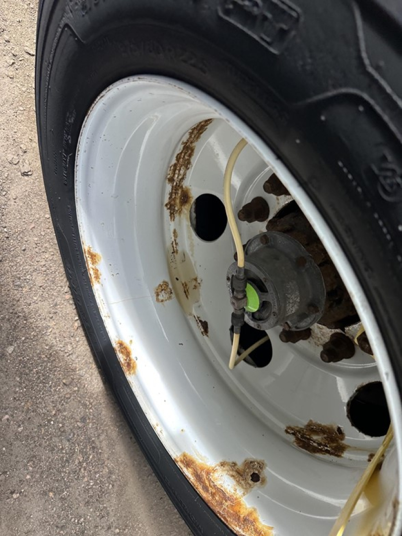Rusted spots on wheel rim and outer edge of a white trailer wheel showing tire, hub, and corroded rim areas.
