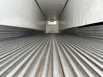 Trailer interior showing ribbed load floor in a refrigerated trailer with white walls and a small rear opening glimpse.