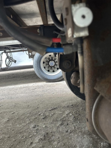 Underbelly view of a 2018 Utility 3000R trailer showing hoses and fittings near the wheel; visible components include a blue and red hose, a steel frame, and a white wheel hub.