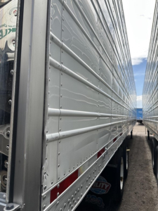 Trailer side view showing aluminum riveted panels of a 2018 Utility 3000R reefer trailer with ribbed siding and visibility of wheels and rear compartments.
