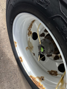 Rusted spots on wheel rim and outer edge of a white trailer wheel showing tire, hub, and corroded rim areas.