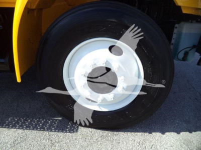 Truck wheel with black tire and white rim, yellow fender in background, blue undercarriage part visible.