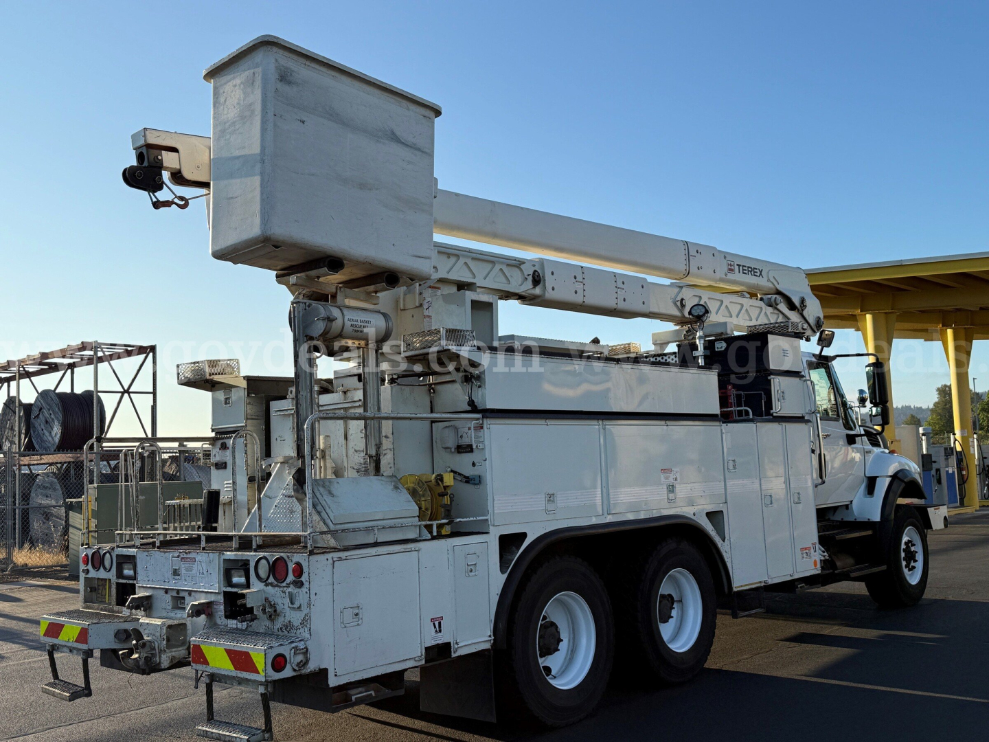 International 7500 bucket truck with aerial lift mounted on chassis, white utility body, bucket stowed, rear platform visible, side mirrors and stabilizers.