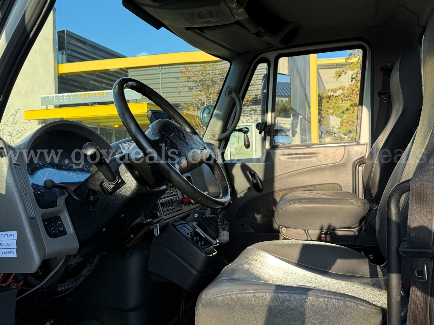 Truck cab interior of a 2010 International 7500 showing steering wheel, dashboard, driver's seat, and passenger seat from the side window view.