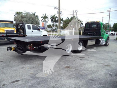 Flatbed rollback truck trailer connected to a green Peterbilt truck in a used vehicle lot.