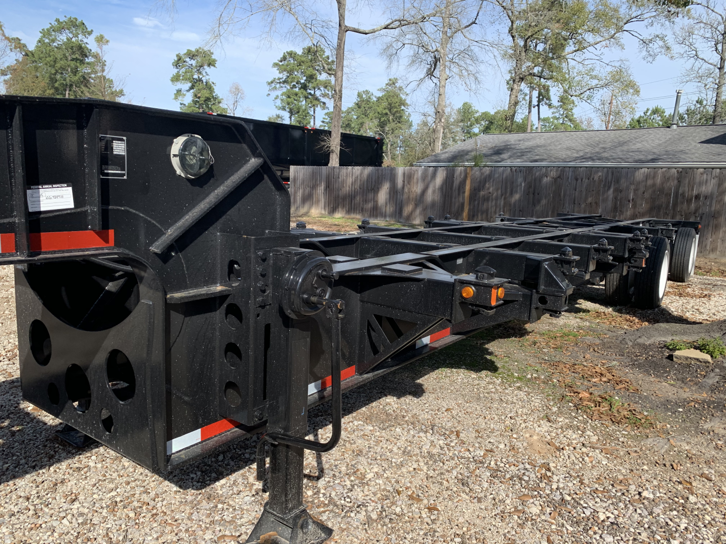 Chassis trailer frame showing heavy-duty black steel with towing hitch and support beams; multiple axles and wheel hubs visible along the length.