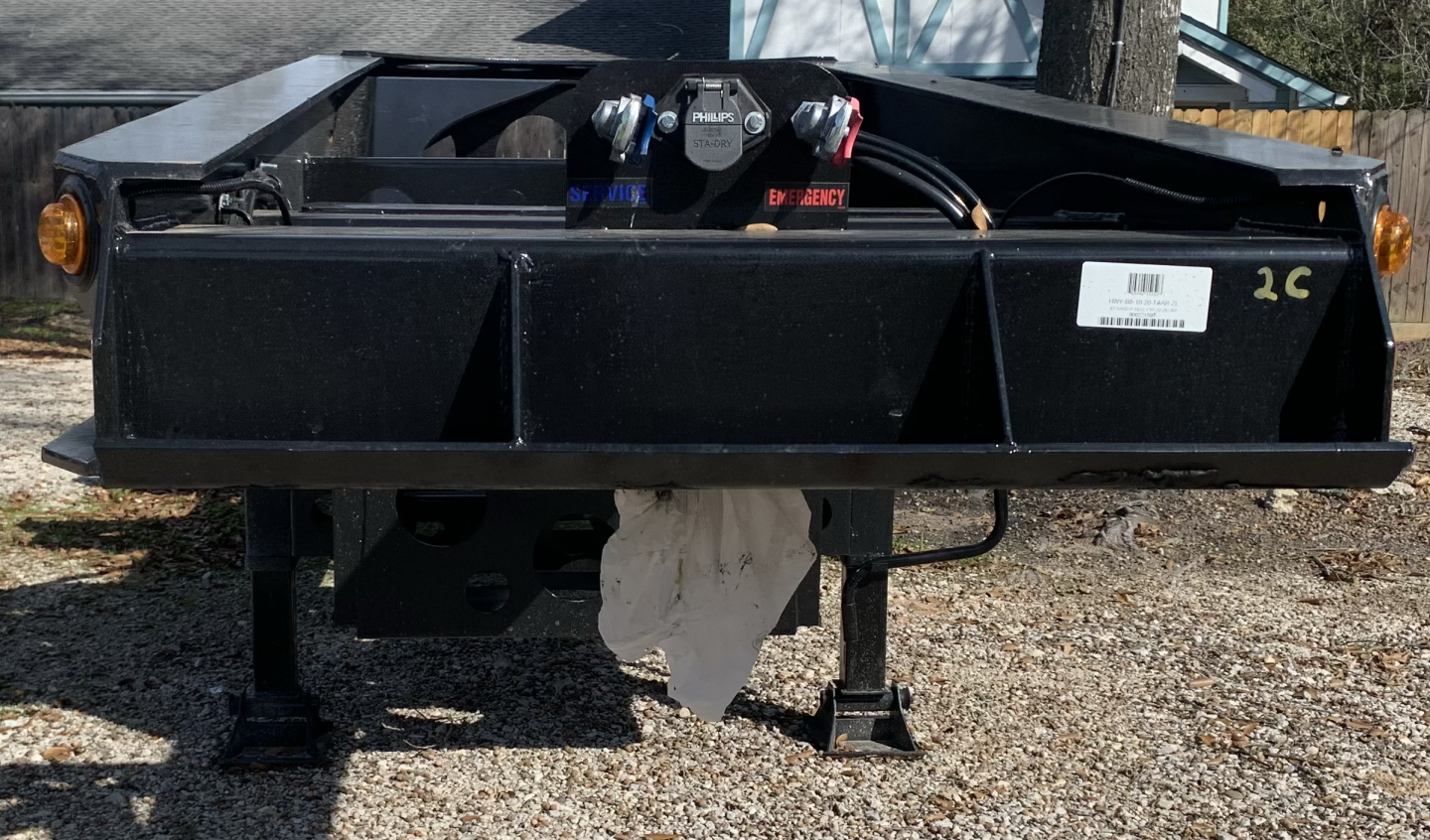 Front view of a black 43' sand chassis trailer showing a central hitch/winch assembly, side marker lights, and a white barcode sticker on the right, with metal support legs visible.