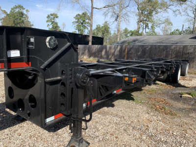 Chassis trailer frame showing heavy-duty black steel with towing hitch and support beams; multiple axles and wheel hubs visible along the length.