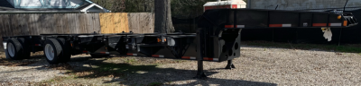 Trailer chassis showing a semi-trailer frame on a gravel lot with support legs and multiple axles visible.