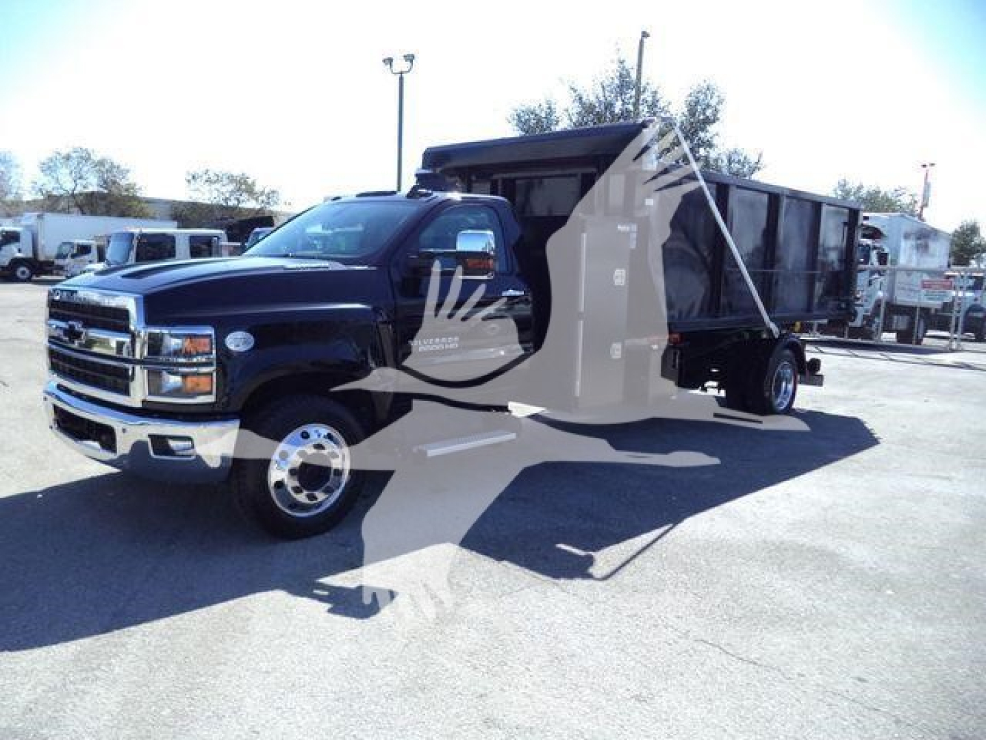 Truck in service bay showing 2023 Chevrolet Silverado 6500HD roll-off dump bed with black cab and large cargo area.