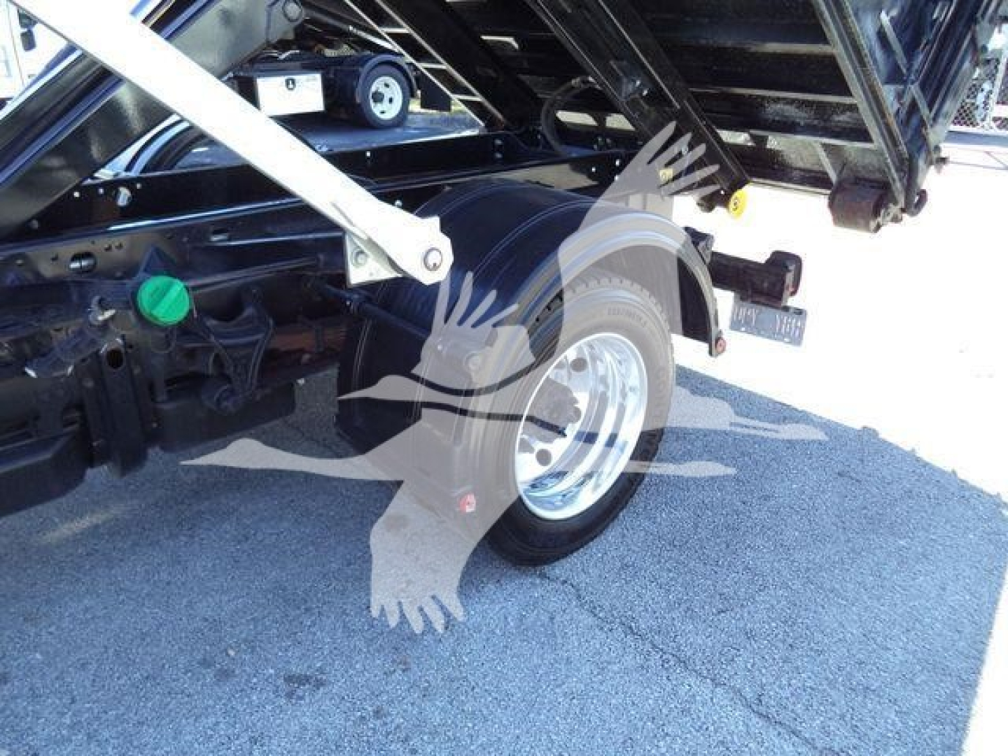 Truck rear wheel and hydraulic components of a 2023 Chevrolet Silverado 6500HD roll-off body showing wheel, fender, green cap reservoir, and undercarriage label.