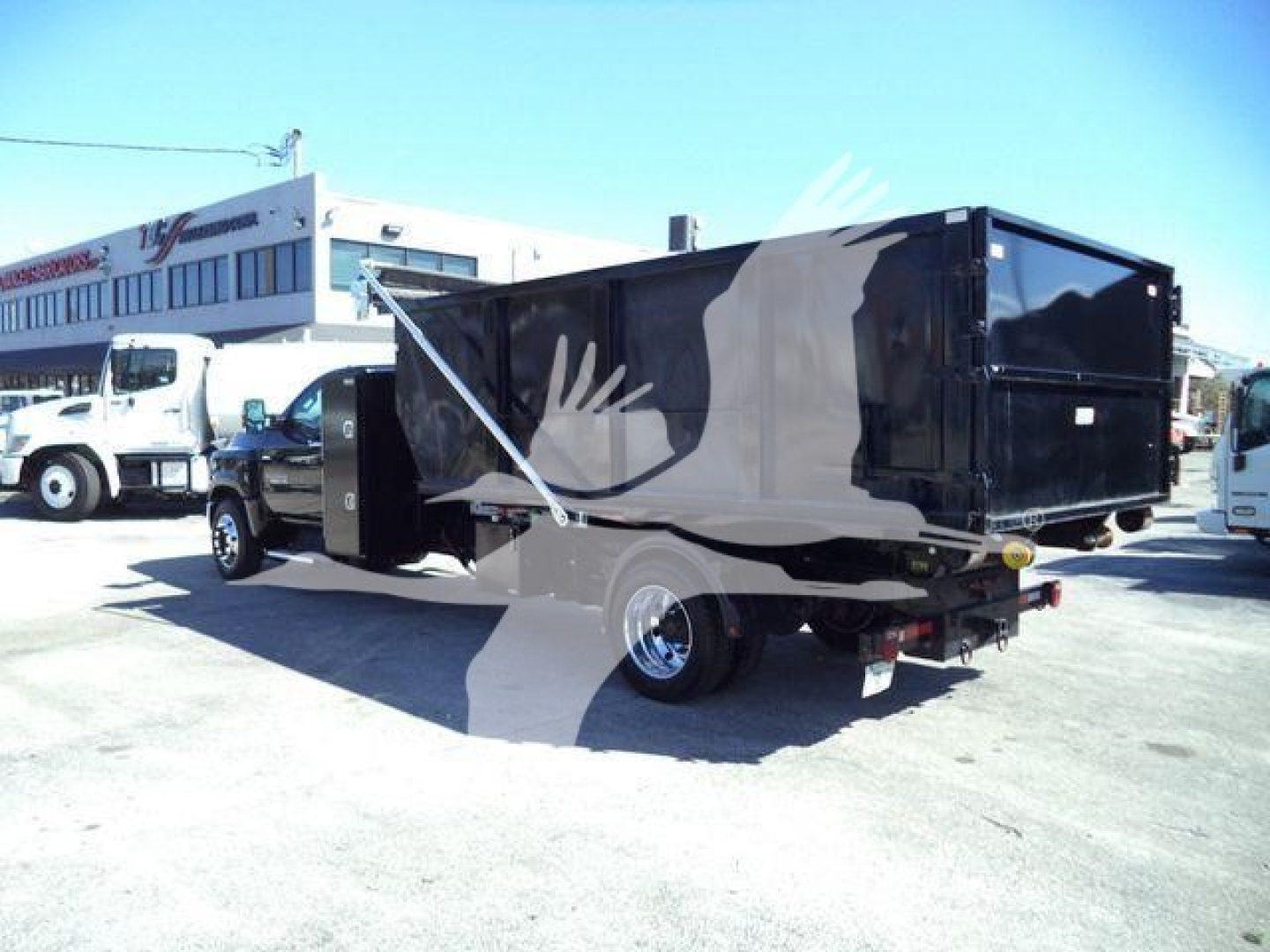 Chevrolet Silverado 6500HD roll-off truck with black dump bed and graphic side, side view showing rear hitch and wheel.