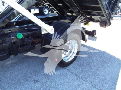 Truck rear wheel and hydraulic components of a 2023 Chevrolet Silverado 6500HD roll-off body showing wheel, fender, green cap reservoir, and undercarriage label.