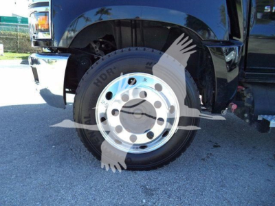 Truck wheel and fender area showing large steel wheel with hub and lug nuts; partial front bumper and tire visible.