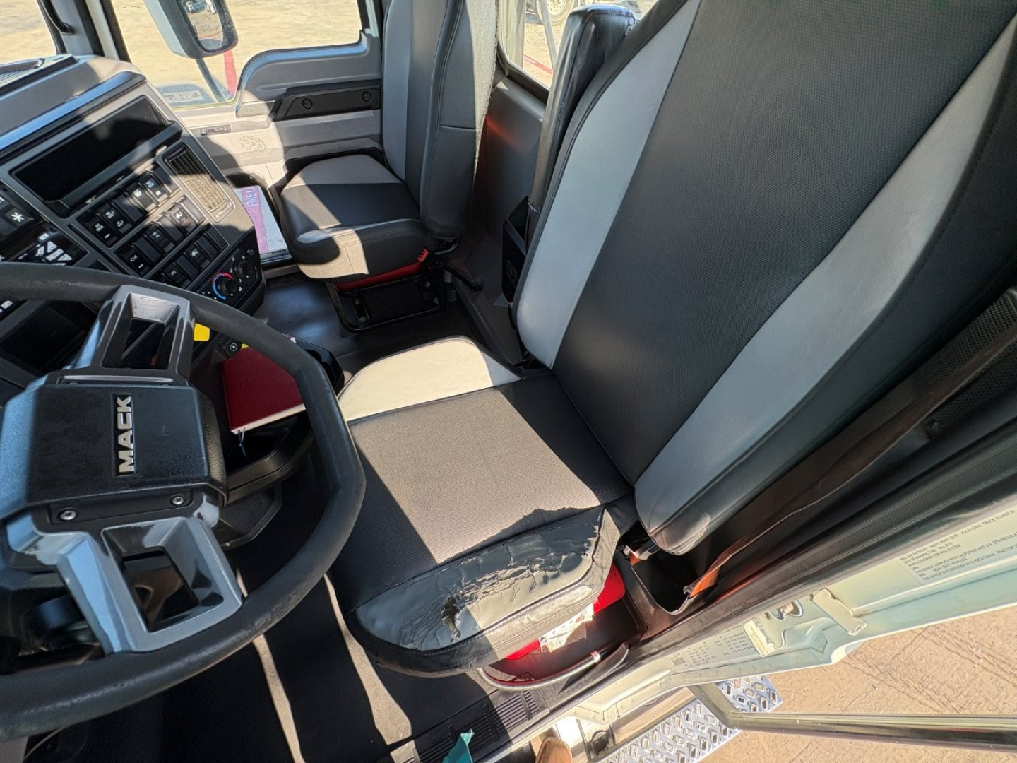 Truck cab interior image showing Mack steering wheel and front seats of a 2020 Mack PI64T daycab.