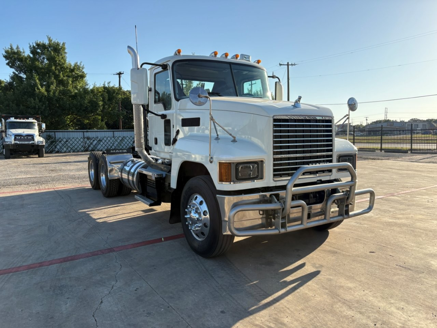 2020 Mack PI64T conventional day cab truck in white, front grille with bumper guard, side mirrors, and orange clearance lights on top. Clear windshield, dual front tires, chassis visible.