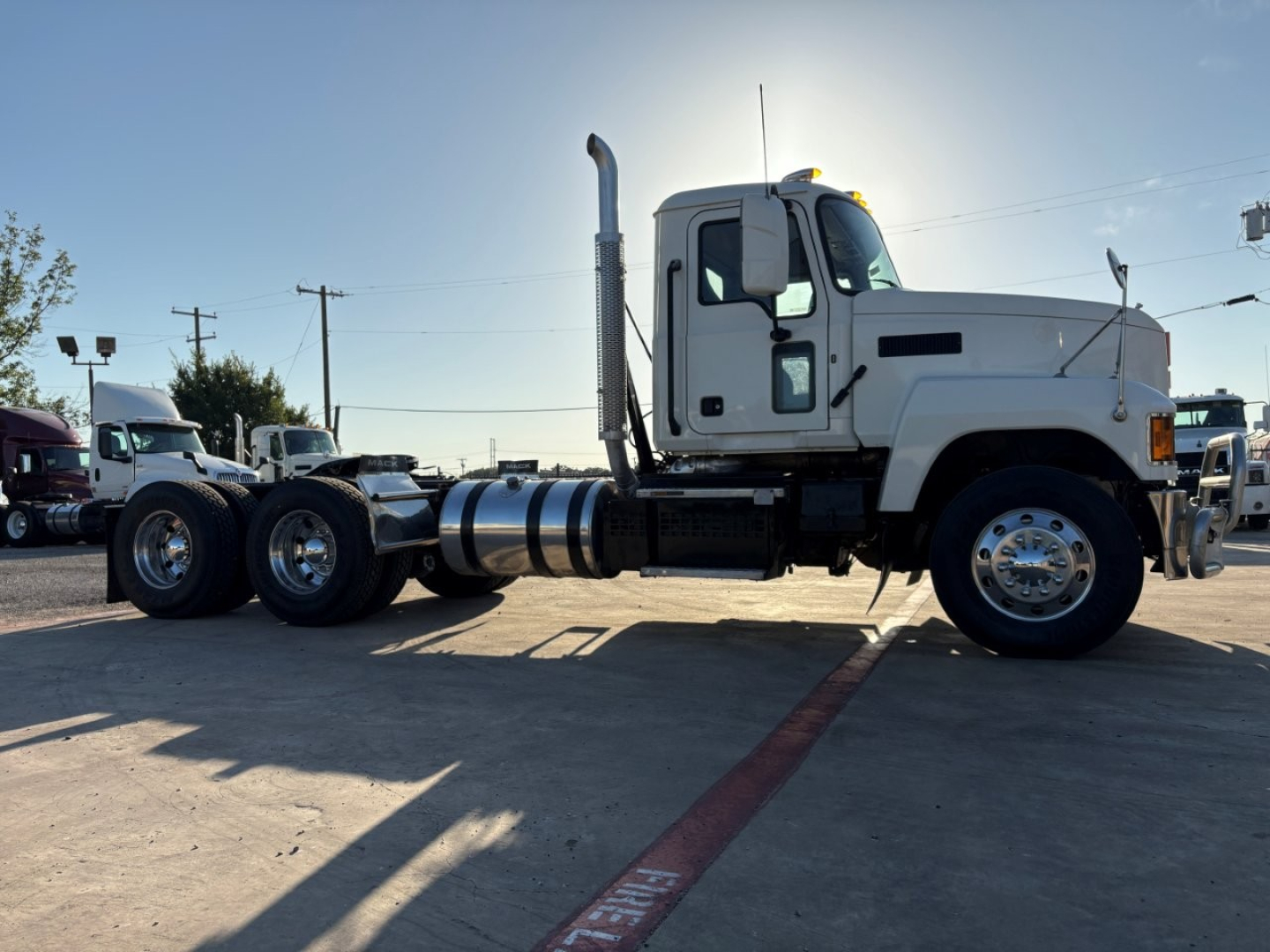 Truck side view showing a white 2020 Mack PI64T conventional daycab with dual rear axles and exhaust stack, fuel tanks, and black chassis.