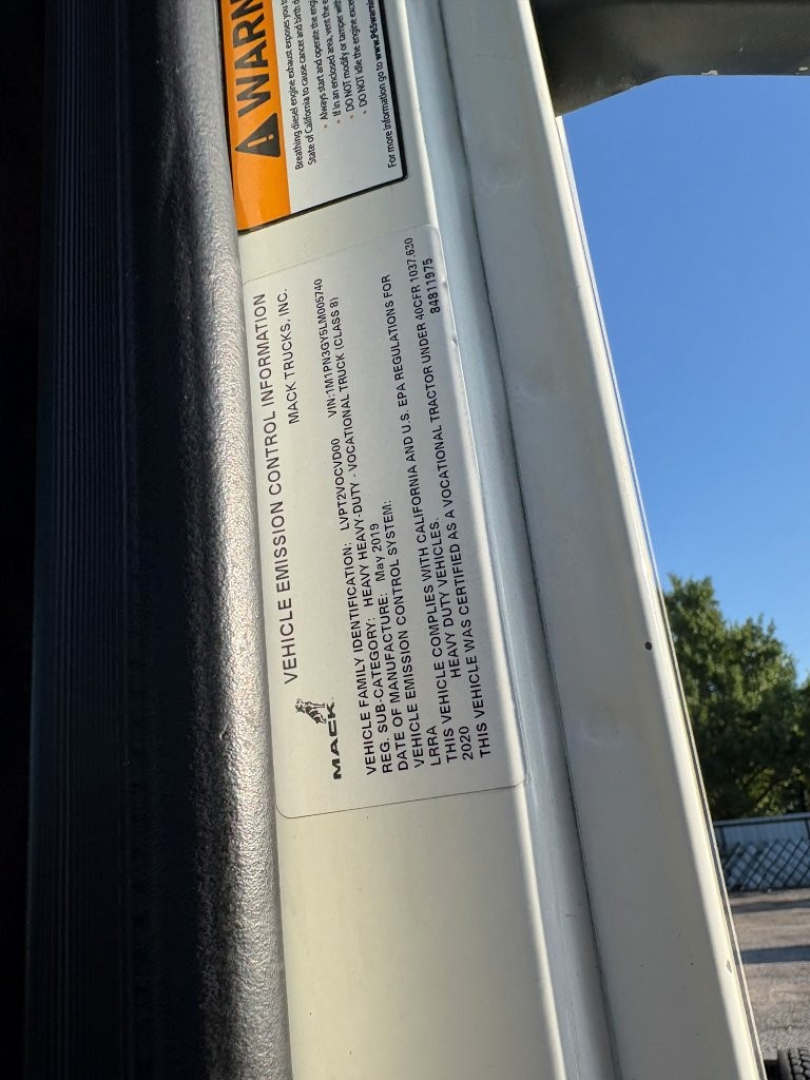 Warning label and vehicle information label on the door of a 2020 Mack PI64T daycab showing vehicle emission information and caution text.