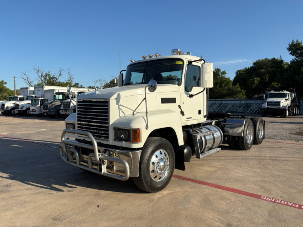 Conventional daycab truck in a lot showing a Mack PI64T with a front bumper guard, grille, headlights, and dual rear axles. Visible text includes fuel tanks and chassis components.