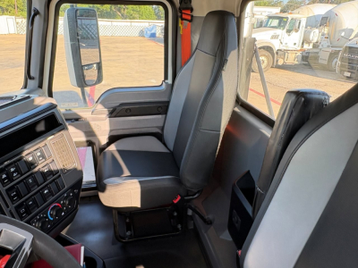 Interior cab view of a 2020 Mack PI64T truck showing driver's seat, passenger seat, dashboard, and window with exterior lot in background.