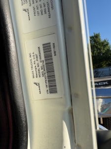 Truck door jamb sticker with VIN and model details; label shows MAC TRUCKS INC, MODEL P1T/150? and serial/barcodes; vertical orientation.