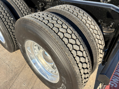 Dual rear tires on a Mack PI64T conventional daycab with chrome wheel, visible tread pattern and suspension components.