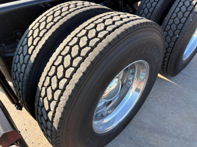 Truck axle dual tires with tread pattern visible, wheel rims and chrome hub, part of a Mack PI64T tractor unit.