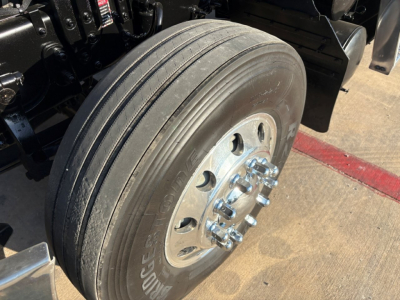 Truck wheel assembly with dual rear tires and chrome lug nut hubcap on a Mack PI64T cab chassis, visible tire treads and front wheel area.