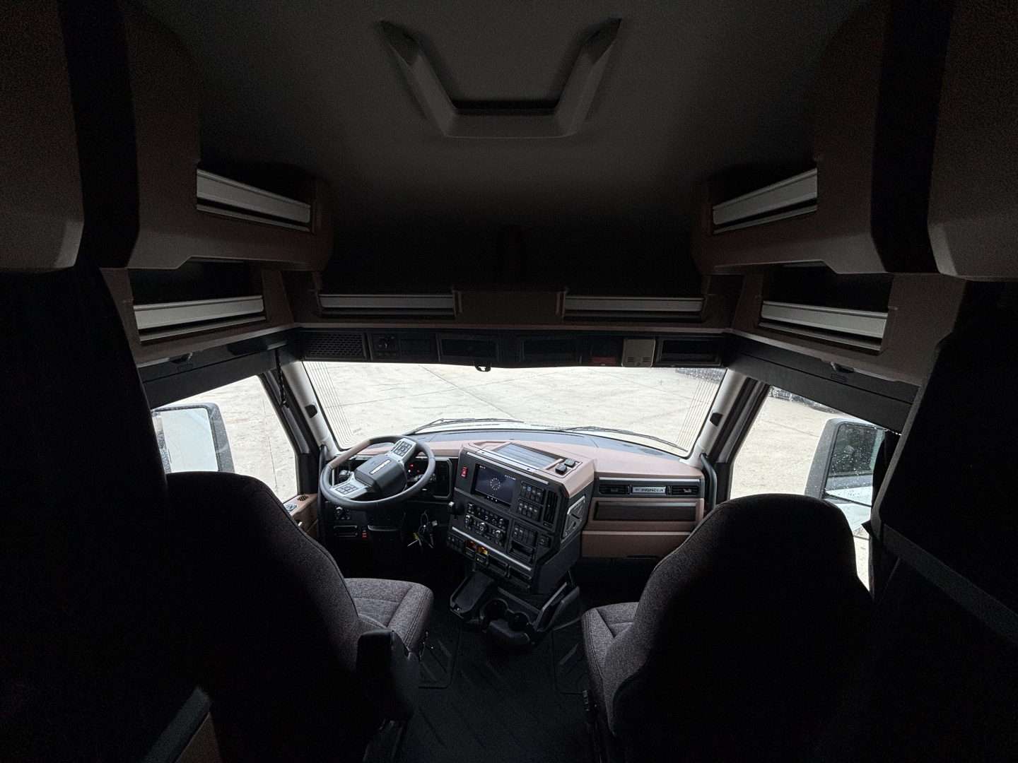 Cab interior of a new Mack PR64T76M truck showing dashboard, steering wheel, and dual captain seats with overhead storage compartments.