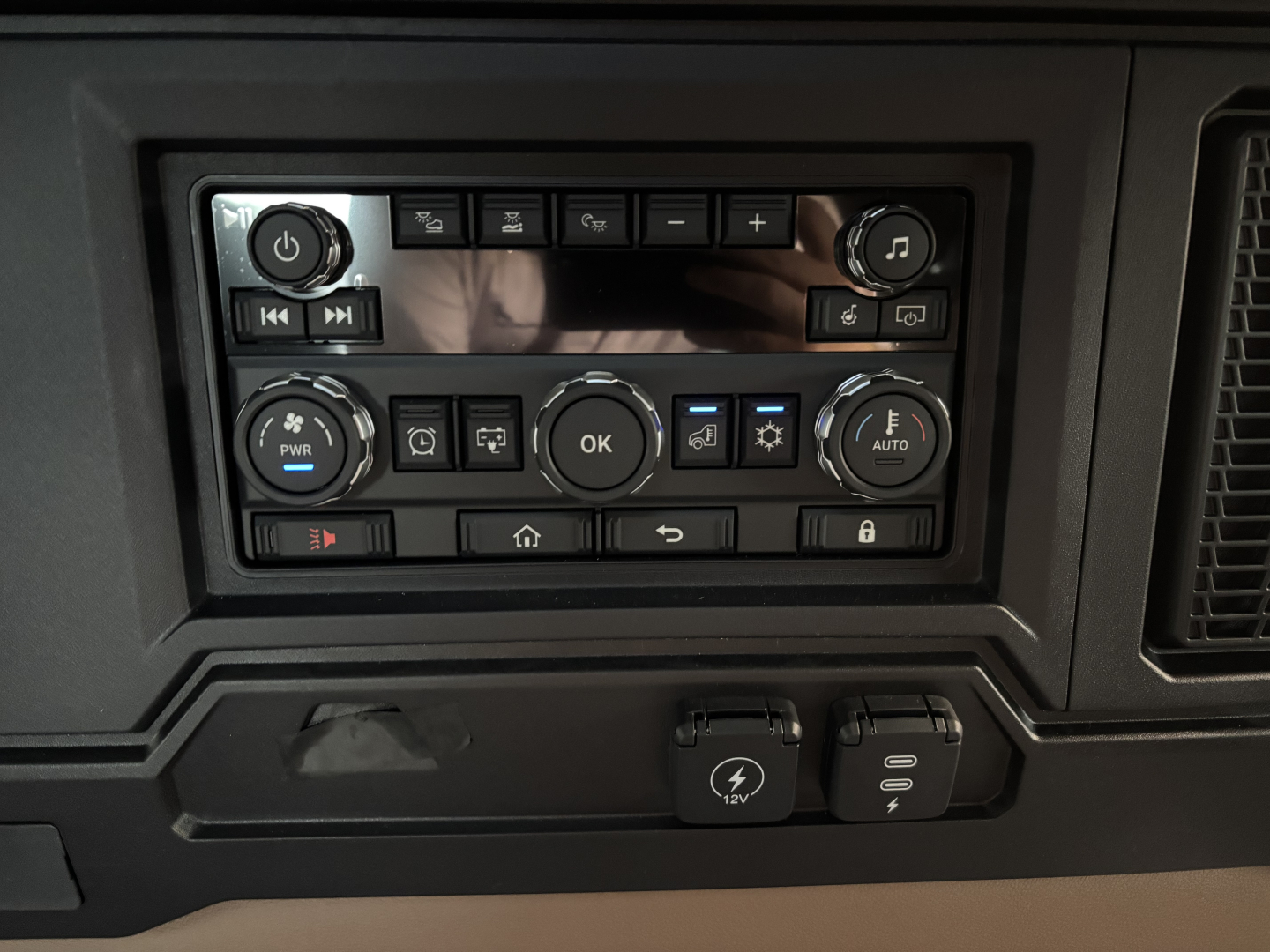Truck interior control panel showing multiple buttons, knobs, and display screen in dashboard area