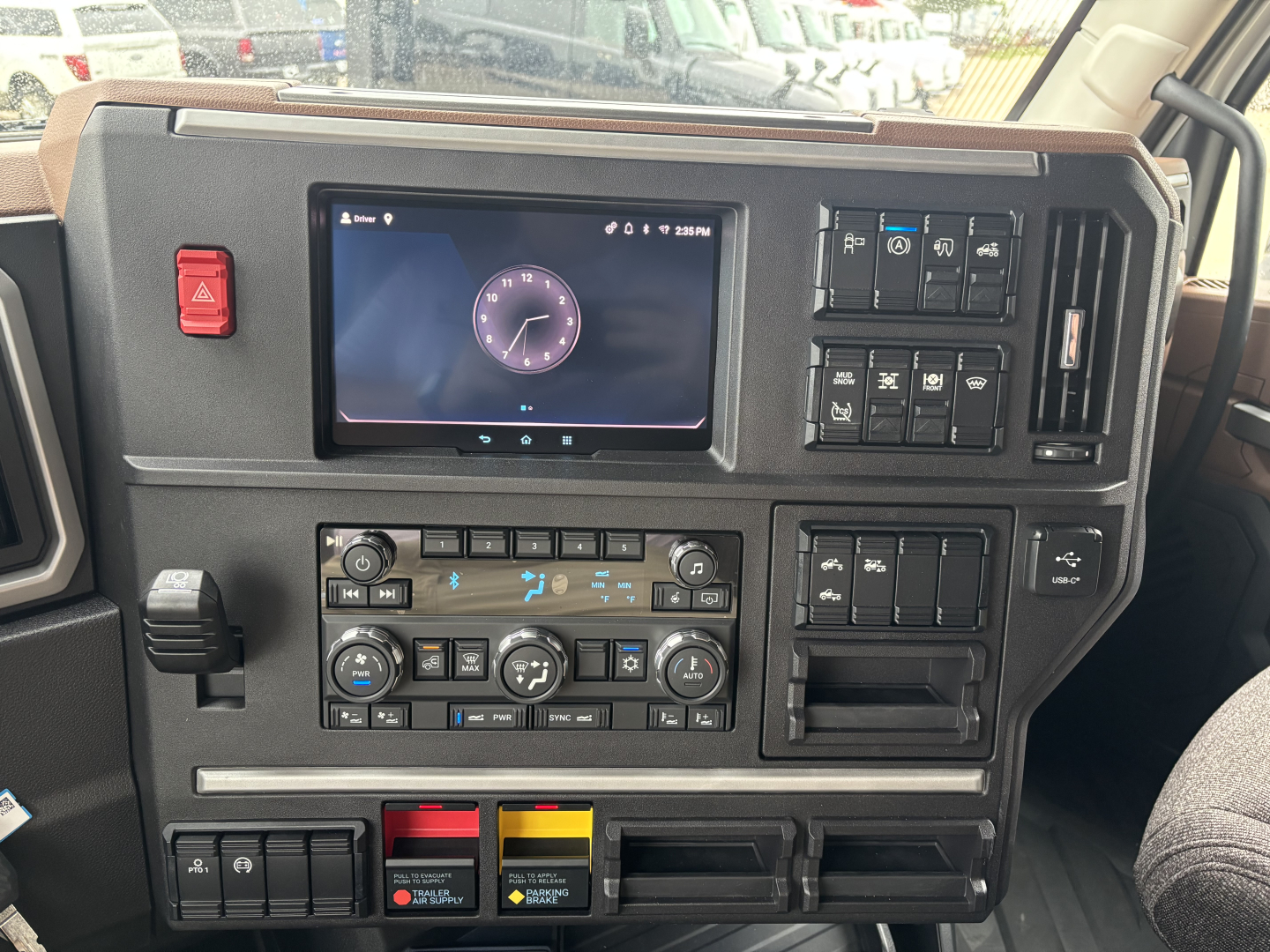 Dashboard view of a 2027 Mack PR64T76M cab interior showing a touchscreen display, climate controls, and various switch panels.