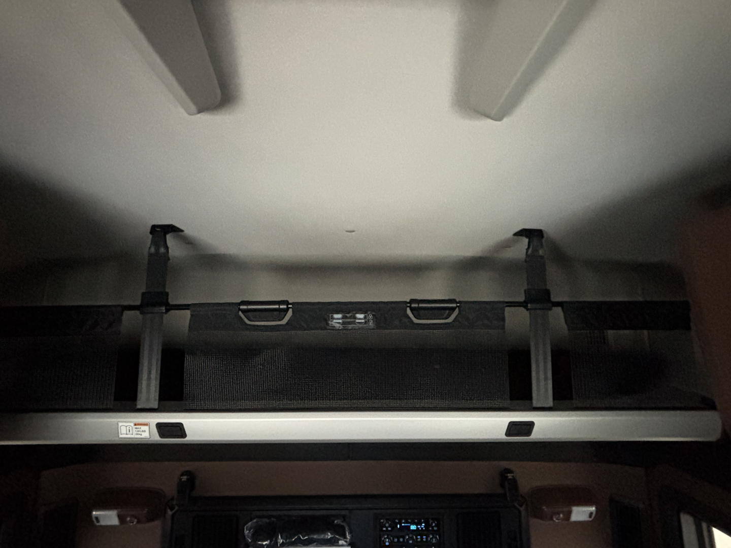 Truck sleeper cab interior showing overhead storage bins and a light bar with two latches, view from bed area.