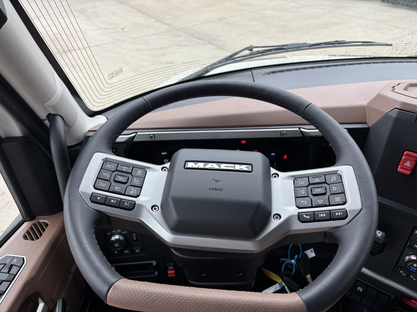 Mack PR64T76M truck interior showing steering wheel and dashboard with control buttons on both sides.