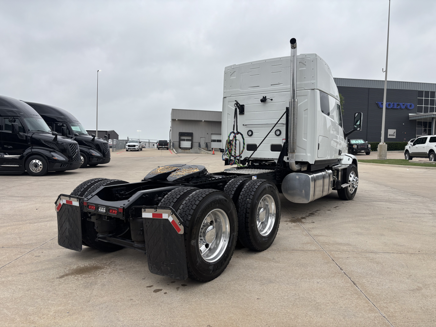 Truck chassis in view showing rear dual-axle configuration and fifth wheel, with white cab and sleeper, Mack PR64T76M model identification not visible on image.
