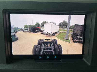 Chassis and fifth wheel shown from cab view in a truck lot; rear wheels and hitch visible with trailers in background