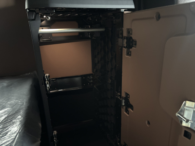 Truck cab interior showing storage cabinet inside sleeper, open cabinet door on right side, shelves and metal rod visible.