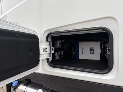 Truck sleeper cab side storage compartment open showing a blue and white stationary equipment device with brand name 'SANTEK' on it inside.