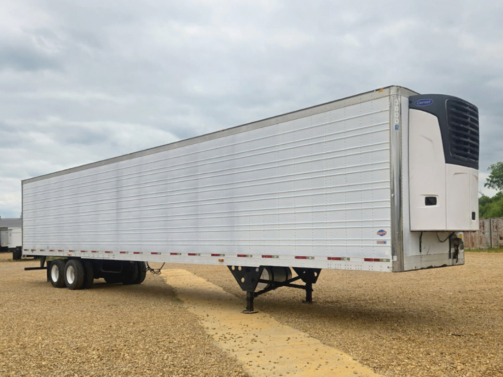 Utility reefer trailer with a white insulated body and a front refrigeration unit, parked on a dirt lot.