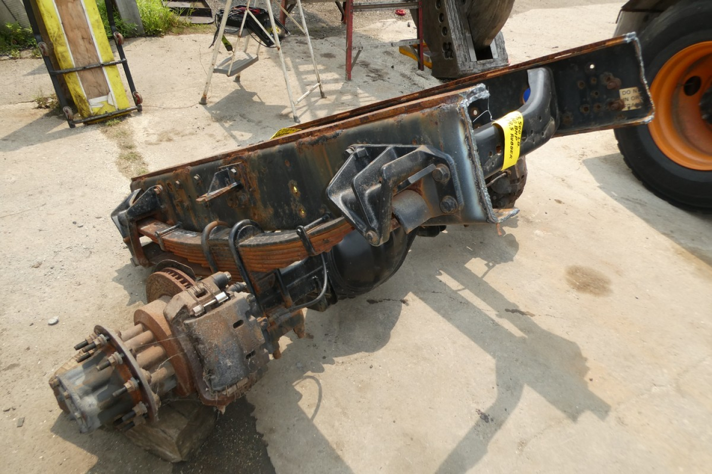 Truck rear axle assembly with rusty frame, brake components, and differential; International Terrastar chassis part lay on ground.