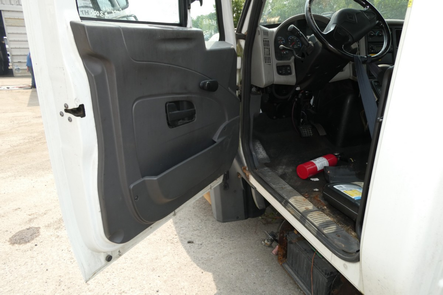 Cab and chassis truck interior showing open front door and driver's area with steering wheel, pedals, and floor; red fire extinguisher on floor near pedals.