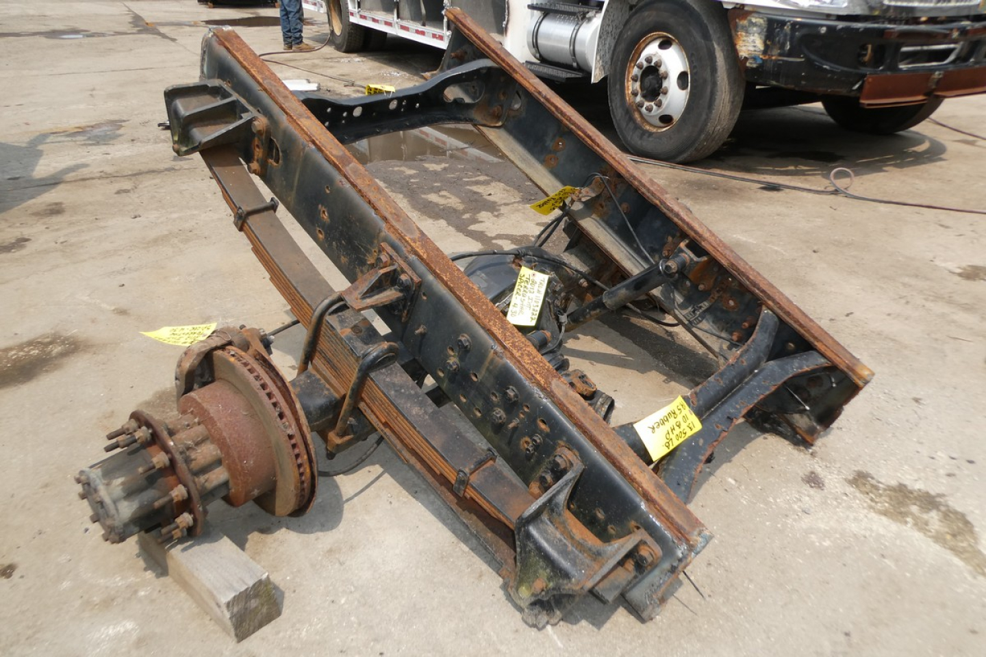 Frame rails and axle housing on a rusty steel truck chassis subframe with wheel hub and drivetrain flange visible.