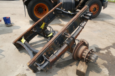 Truck chassis frame with differential and axle components attached, viewed from above, with orange wheels in background.