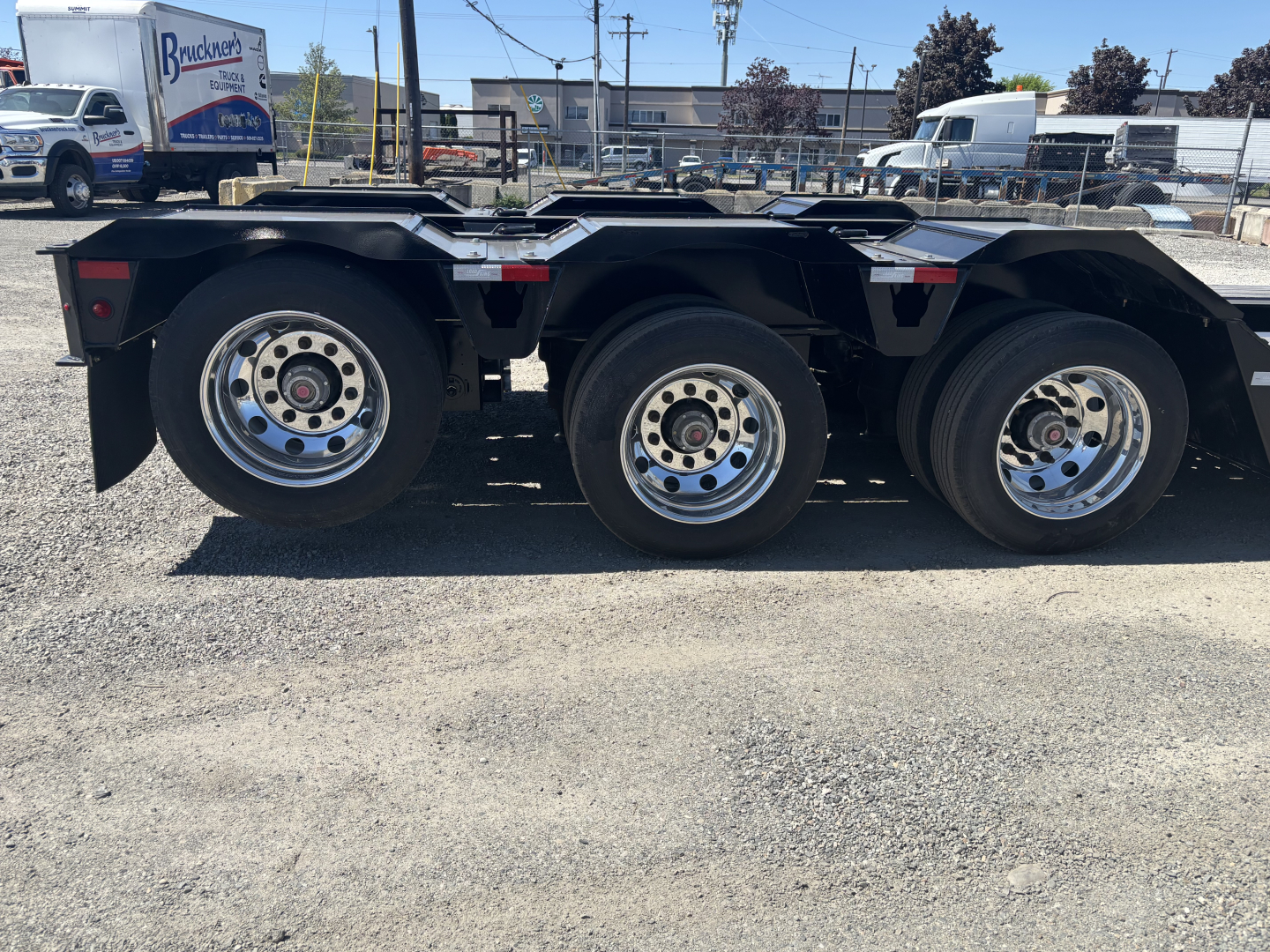 Trailer axle section showing three axles with chrome wheels and black frame, Load King 9' x 24' lowboy trailer in view.